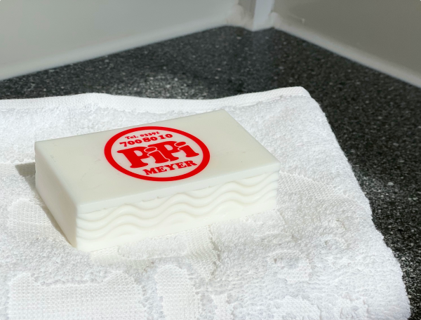 Ein Stück Seife mit dem Logo von Pipi Meyer liegt auf einem weißen Handtuch, platziert auf einer dunklen Oberfläche.