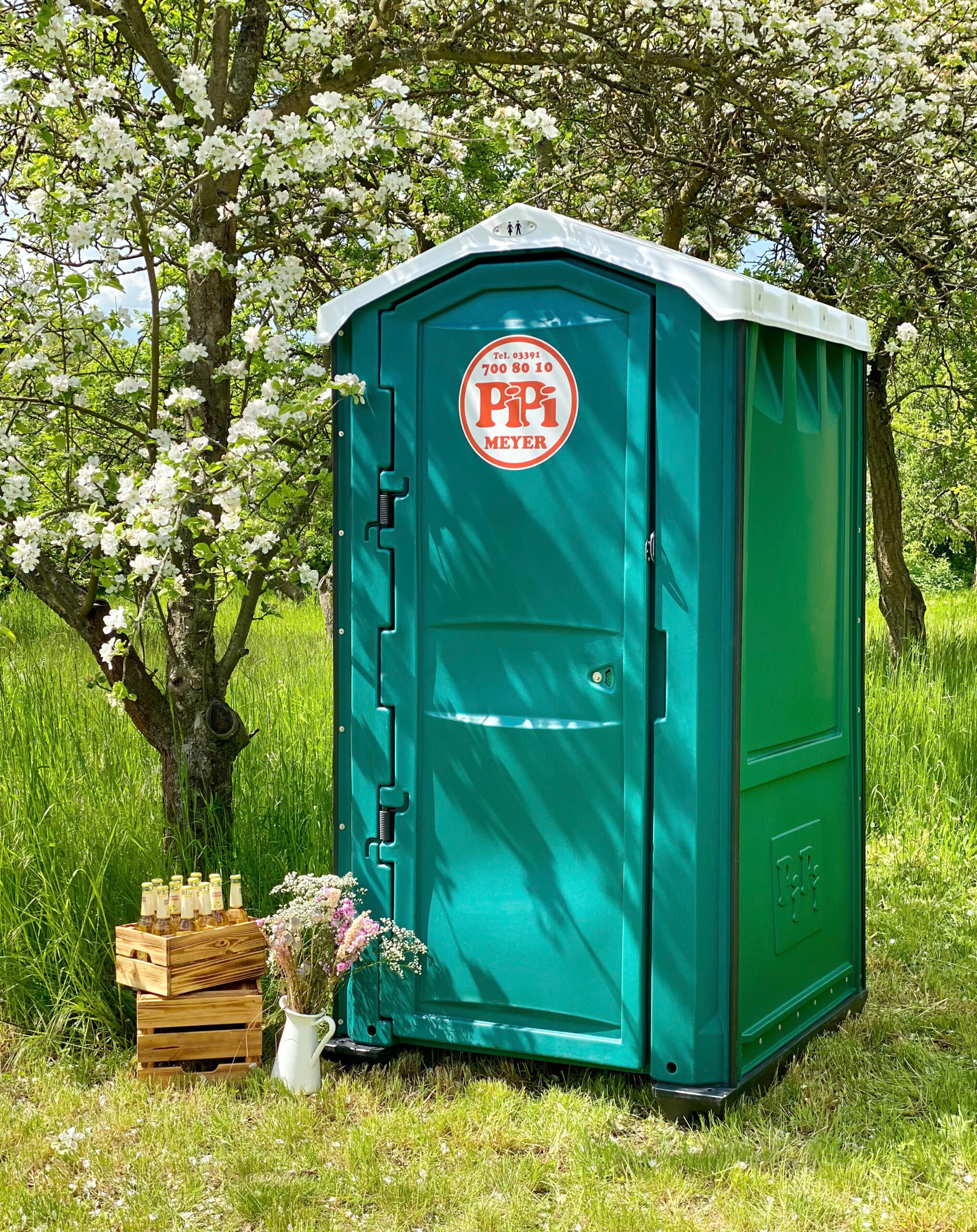 Die PiPiBox Party steht in einem Garten, neben einem Baum.